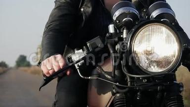 一个穿着黑色皮夹克骑摩托车在乡间小路上的不可辨认男子的正面景色。 大灯打开了